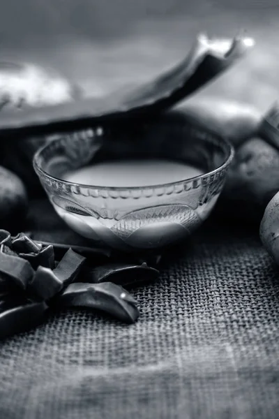 potatoes juice well mixed with aloe vera gel in glass bowl along raw potatoes and aloe vera leaves on jute bag surface, concept  of homemade conditioner and shampoo for dandruff and scalp cleaning