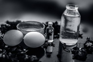 koyu yüzeyde gül yaprakları ile yumurta ve kase ile hint ve hindistan cevizi yağı ile şişeler, kepek mücadele için malzemeler 