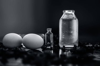 koyu yüzeyde gül yaprakları ile yumurta ve kase ile hint ve hindistan cevizi yağı ile şişeler, kepek mücadele için malzemeler 