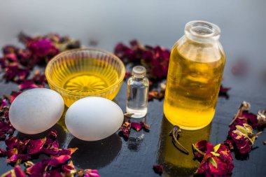 koyu yüzeyde gül yaprakları ile yumurta ve kase ile hint ve hindistan cevizi yağı ile şişeler, kepek mücadele için malzemeler 