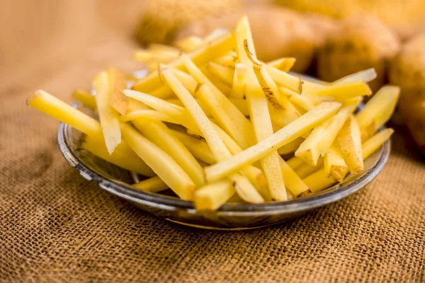 cut french fries in glass plate with raw potatoes on burlap surface