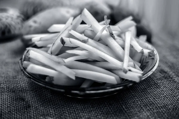 cut french fries in glass plate with raw potatoes on burlap surface