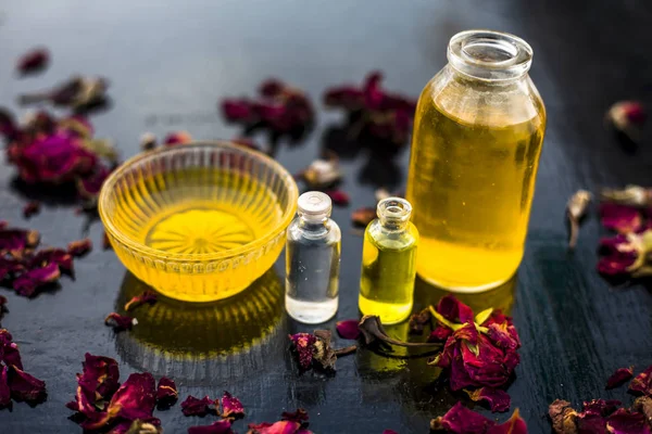 castor oil and tea tree oil with coconut oil in bottles and bowl with raw honey and rose petals on wooden surface