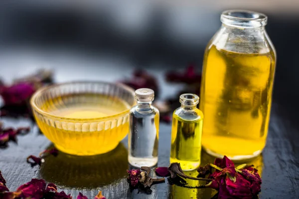 castor oil and tea tree oil with coconut oil in bottles and bowl with raw honey and rose petals on wooden surface