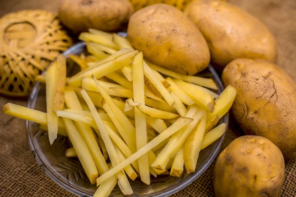 cut french fries in glass plate with raw potatoes on burlap surface