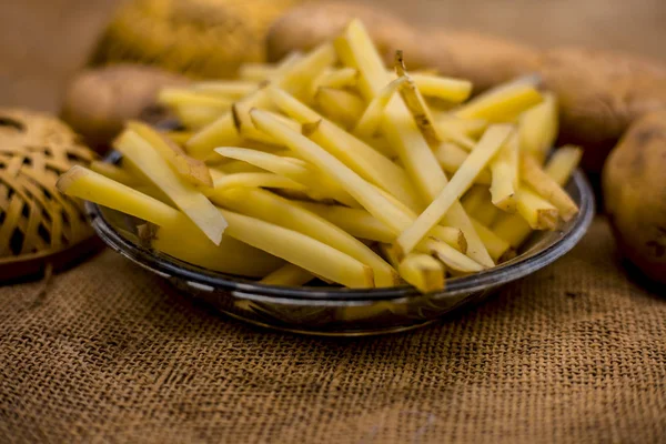 cut french fries in glass plate with raw potatoes on burlap surface