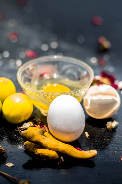 lemons and raw turmeric with egg in glass bowl along with entire raw ingredients for preparation face mask to acne-prone skin on wooden surface