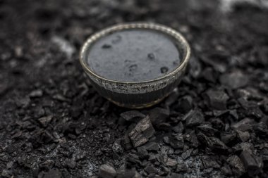 Close up of activated charcoal in a glass bowl on the wooden surface along with some raw powder of charcoal or coal spread on the surface. clipart