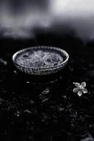 Close up of activated charcoal in a glass bowl on the wooden surface along with some raw powder of charcoal or coal spread on the surface.