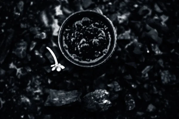 Close up of activated charcoal in a glass bowl on the wooden surface along with some raw powder of charcoal or coal spread on the surface.