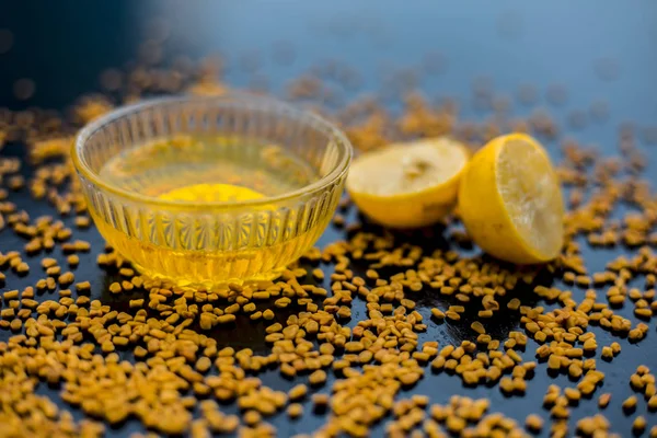 natural hair conditioner for dandruff consisting of fenugreek seeds powder well mixed with lemon juice in glass bowl with raw lemons and fenugreek seeds on wooden surface
