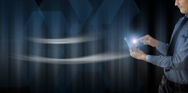 Yakın genç teknoloji / işadamı da bazı astarları ile mavi renkli bir arka plan karşı cep telefonu tutan kadar. Cep telefonu da dokunmatik gösteren kızdırma ile.