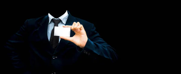 Unrecognizable faceless gentleman or seller holding white colored card in his hand wearing a dark blue colored suit with black necktie isolated on black.Concept of marketting.