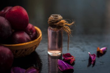 Şeffaf bir cam şişe de çıkarılan uçucu yağ ile birlikte kahverengi renkli sepet içinde Ham organik kırmızı olgun erik.