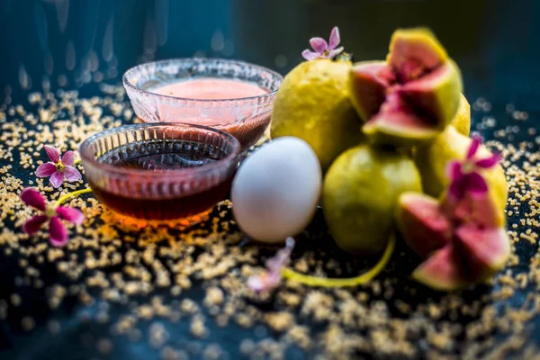 Treatment of dry skin with the help of face mask on a wooden surface consisting of honey, guava pulp, egg yolk, and some oatmeal, well mixed in a glass bowl along with raw ingredients.