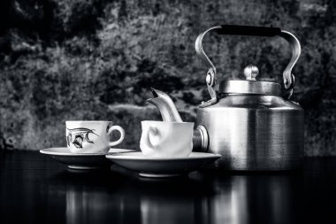 Siyah ve beyaz gotik renklerile siyah renkli parlayan yüzey üzerinde antika su ısıtıcısı ve cam seti ile natürmort. Natürmort kavramı.