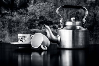 Siyah ve beyaz gotik renklerile siyah renkli parlayan yüzey üzerinde antika su ısıtıcısı ve cam seti ile natürmort. Natürmort kavramı.