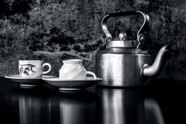 Siyah ve beyaz gotik renklerile siyah renkli parlayan yüzey üzerinde antika su ısıtıcısı ve cam seti ile natürmort. Natürmort kavramı.