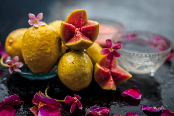 Guava pulp and water well mixed in a glass bowl on the wooden surface along with some raw cut guava, with some rose petals, also completing a face mask used for a natural glow.
