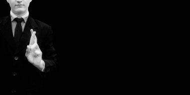 Siyah renkli bir arka plan üzerinde izole elleri ile iyi şanslar işareti yapıyor takım elbiseli işadamı.