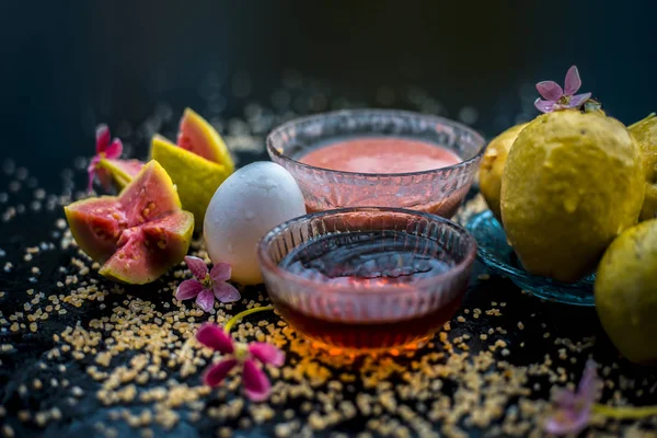 Guava face mask for dry skin on a wooden surface with vivid colors i.e., guava pulp, egg yolk, oatmeal, and some raw organic honey well mixed in a glass bowl along with raw ones.