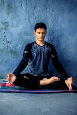 Genç enerjik erkek genç model Sukhasana poz veya renkli bir paspas üzerinde beyaz bir arka plan üzerinde izole kolay poz yapıyor.