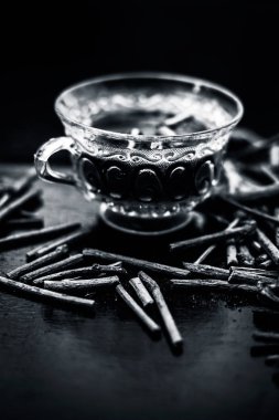 Bir cam bardak çayı ile de manjistha / manzistha / Rubia cordifolia / madder vb olarak bilinen siyah ahşap yüzeyüzerinde kahverengi renkli sepet Hint madderwort veya madder kök Demet. Dikey çekim.