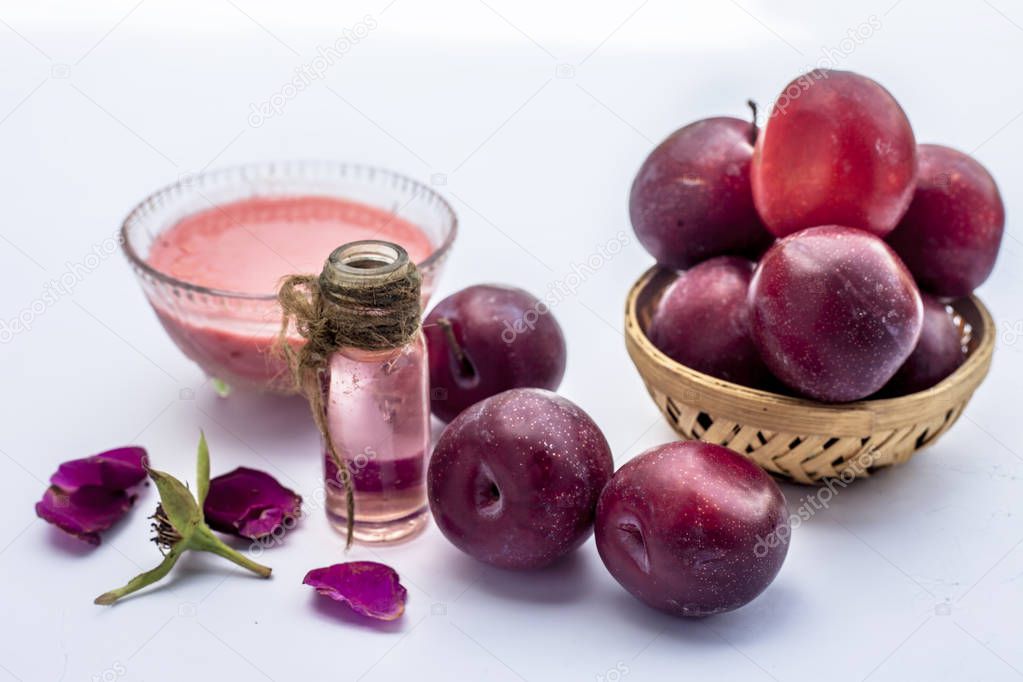 Fresh ripe plum along with its face mask consisting of some plum pulp and rose water in glass mini bottle isolated on white.