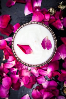 Taze süt, cam kasede gül suyuyla karıştırılmış ahşap yüzeyde yapraklarla.