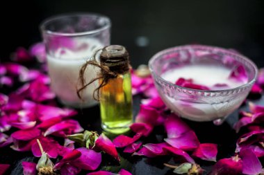 Gül sütü, süt kremi ve zeytin yağını içeren yüz bakımı ahşap yüzeyde cam bir kâse ve bazı gül yapraklarıyla birlikte..