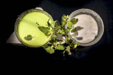 Tulsi ya da fesleğen yapraklarından oluşan bitkisel ve ayurvedik yüz maskesi bir cam kasede, ahşap yüzeyde kaymak ve çiğ tül yapraklarıyla karıştırılmış bir tül özünden oluşur..