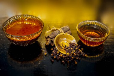 Tarçın, bal ve karanfil saç maskesi, cam bir kasede, ahşap bir yüzeyde, izole edilmiş altın ışıklarla. Yüzeyde duran çiğ tarçın çubuğuyla birlikte tatlım..