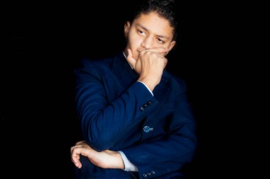 Derin düşüncelere sahip kafası karışmış bir iş adamı, mavi bir davada siyah bir arkaplanda poz veriyor..