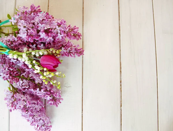 Beyaz ahşap masa, yan alan leylak, lale, beyaz lavanta, yeşil bir şerit ile bağlı oluşan bir buket ile dekore edilmiş