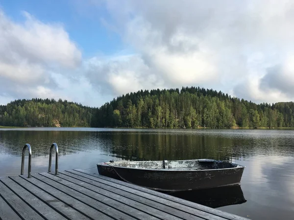 the boat is tied next to a wooden pier, smooth clear water of the lake, the shore covered with forest, autumn, Karelian nature, reflection in the water