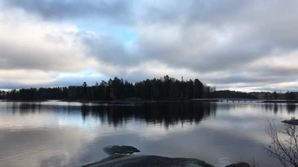 大きな平たい石が針葉樹と島の前の湖に入る美しい秋の空 フィンランドの自然に反映されます — ストック動画