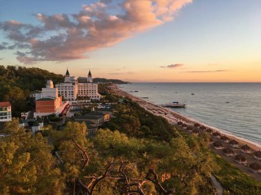 Türkiye, Kemer, 28 Ekim 2018. güzel Türk otel çevrili yeşil, relict çam ağaçları, deniz, plaj, şafak, bulutlar, otel binası kuleli, üst düzeyde geri kalanı tarafından. Amara Dolce Vita lüks
