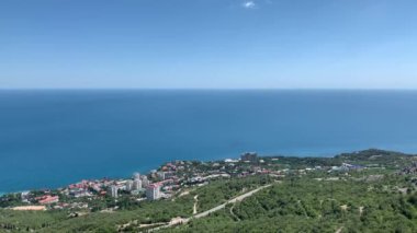 Deniz kıyısının yüksekliğinden manzara, bir sürü yeşillik, küçük binalar, yol, mavi deniz, açık güneşli gün