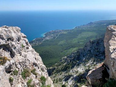 Bir dağın yüksekliğinden mavi deniz manzarası, bir uçurum, birkaç ağaç, kayalar, dolambaçlı bir kıyı şeridi, dinlenmek için şık bir yer.