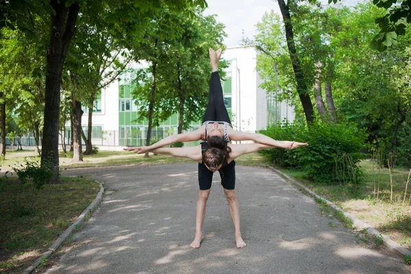 Young athletic couple practicing acroyoga in park outdoors urban style.Balancing in pair. Fit active pair yoga time.Sporty handsome man supporting slim beautiful brunette woman.Training time.Asana