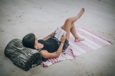 Kitap okuma tropikal kumsalda yatıp güzel ve genç birbayan. Koh Tao, Tayland