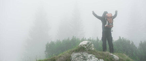 Hiking man with backpack open arms on foggy mountain peak. Durmitor, Montenegro