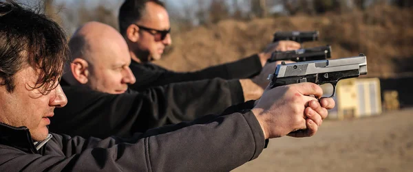 Group of people practice gun shoot on target on outdoor shooting range. Civilian team weapons training