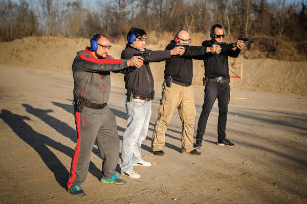 Group of people practice gun shoot on target on outdoor shooting range. Civilian team weapons training