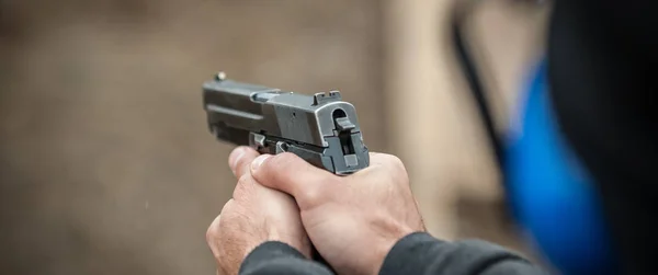 Detail view of shooter holding gun in hand and shooting, close up. Shooting range