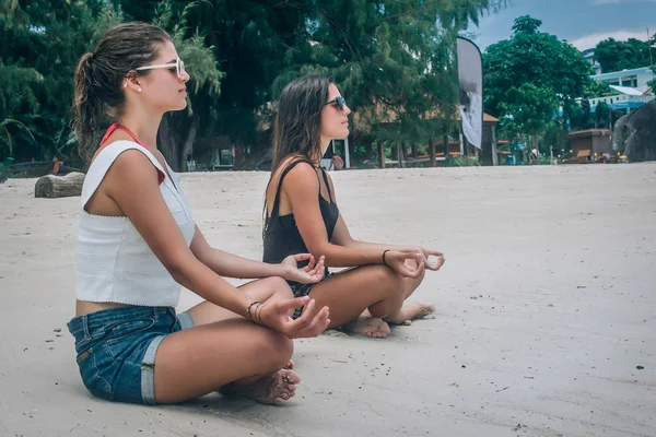 Dos amigas haciendo yoga posan en la playa en posición de loto —  Fotos de Stock