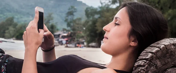 Junge Frau mit Smartphone entspannt am tropischen Strand — Stockfoto