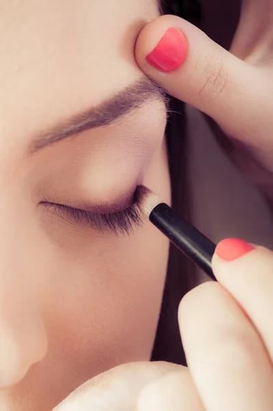 Primer plano de las manos aplicando polvo de sombra de ojos sobre la piel facial femenina — Foto de Stock