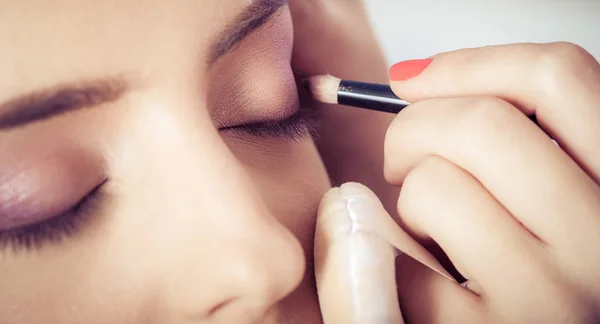 Primer plano de las manos aplicando polvo de sombra de ojos sobre la piel facial femenina — Foto de Stock