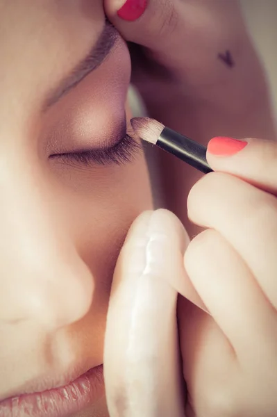 Primer plano de las manos aplicando polvo de sombra de ojos sobre la piel facial femenina — Foto de Stock